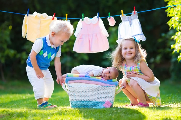 Newborn child on a pile of clean dry towels. Brother and sister kissing little sibling. Siblings bonding. Kids and baby clothing on laundry line and basket. Children playing outdoors in summer garden