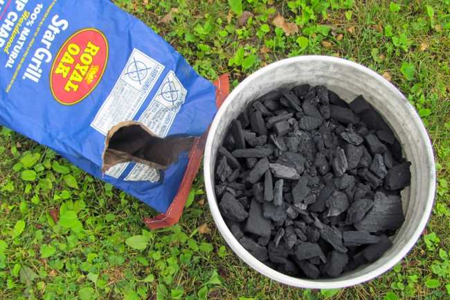 Un sac de charbon de bois vide à côté d'un seau rempli de charbon de bois en morceaux