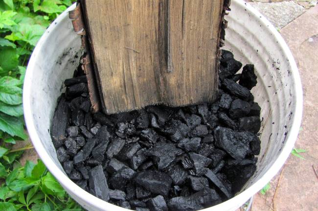 un seau rempli de charbon humide et un morceau de bois servant à réduire le charbon en morceaux plus petits