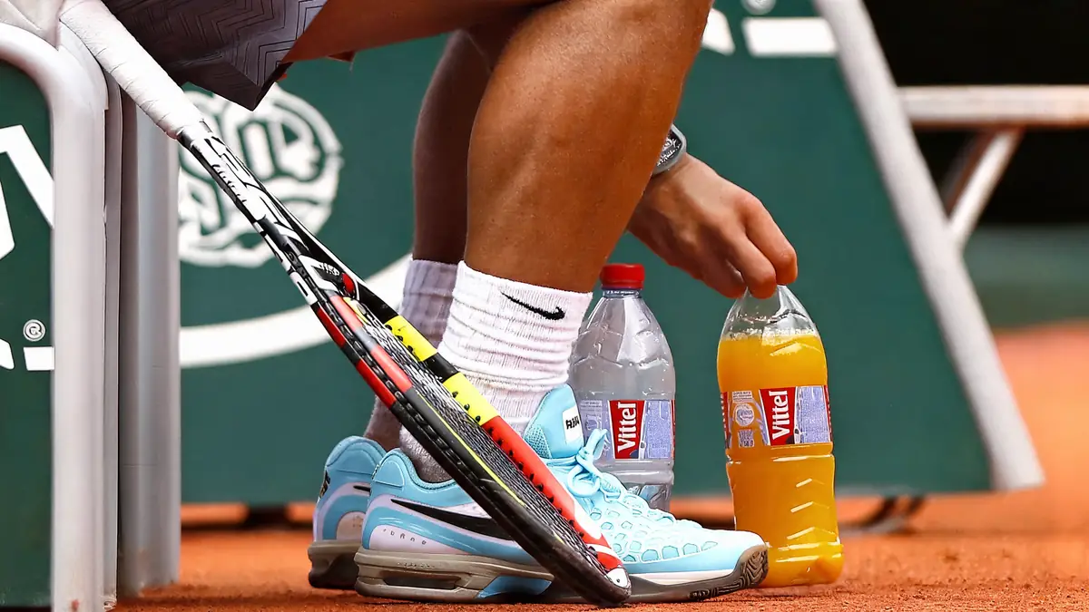 Un joueur de tennis assis avec sa raquette et sa boisson pour le tennis sur le court