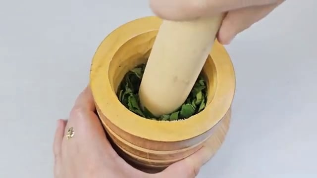 Les feuilles hachées sont écrasées dans un mortier avec un pilon pour en extraire le jus vert.