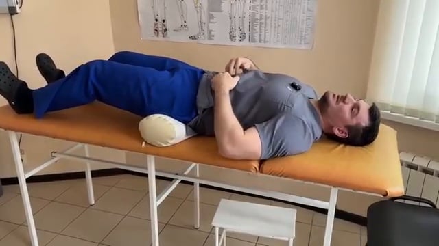 Démonstration de l'exercice de bascule du bassin : le thérapeute presse le bas du dos contre la table tout en contractant les abdominaux.